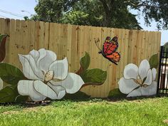 a fence painted with white flowers and a butterfly on it, in front of a wooden fence