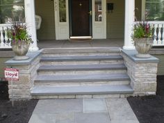 a front porch with steps leading up to the door and flower pots on either side