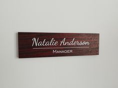 a wooden sign that says natalie anderson manager on it's side in front of a white wall