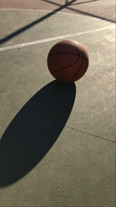 a basketball sitting on top of a court next to a net with the shadow of it's ball