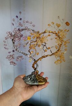 a hand holding a piece of metal and gold wire with flowers on it in front of a wall