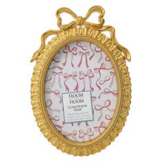 an ornate gold frame with pink ribbon on the front and bottom, hanging from a white wall