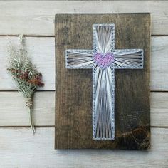 a cross with a pink heart on it next to some dried flowers and a wooden board