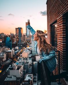 a woman standing on top of a building with her arms in the air and looking out over a city