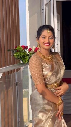 a woman in a gold and white sari standing next to a window with flowers