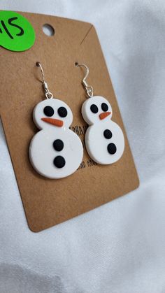 a pair of snowman earrings with black and white dots on them, hanging from a brown card