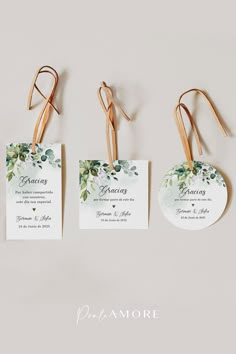 three tags with flowers and leaves on them hanging from the side of a white wall