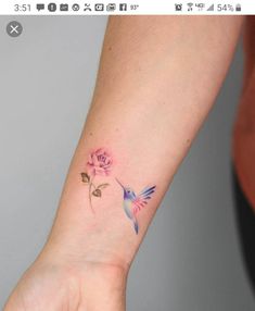 a small tattoo on the wrist of a woman with a hummingbird and pink rose