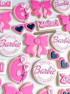 cookies decorated with pink and blue icing are arranged on a white surface, including one cookie that says barbie