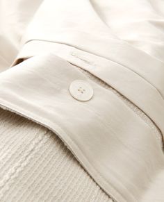 a close up of a white shirt with buttons on the collar and sleeves, laying on top of a bed