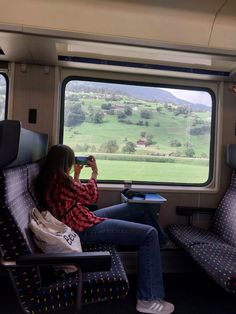 a woman sitting on a train looking out the window at rolling green hills and fields