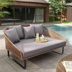 a wicker couch sitting on top of a patio next to a swimming pool with drinks in front of it