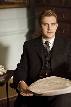 a man in a suit and tie sitting down holding a plate with writing on it