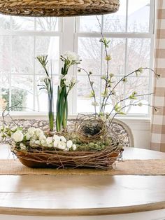 a bird nest with flowers and greenery on a table in front of a window