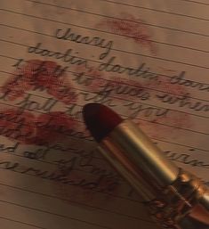 a close up of a lipstick on top of a piece of paper with writing in the background