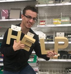 a young man holding up two cardboard letters that spell the word hlp in front of him