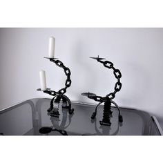 two candles are chained to each other on a glass table with white wall in the background