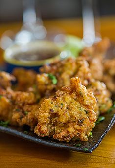 some fried food on a black plate with dipping sauce in the bowl next to it