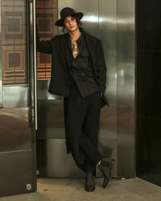 a man standing in front of an elevator with his hand on his hip and wearing a black hat