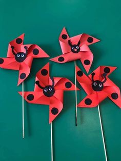 four red and black pinwheels with ladybugs on them sitting on a green surface