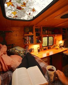 a person sitting in a bed with their feet up on a book and holding a cup