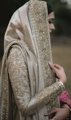 a woman in a white and gold bridal outfit is holding another woman's hand