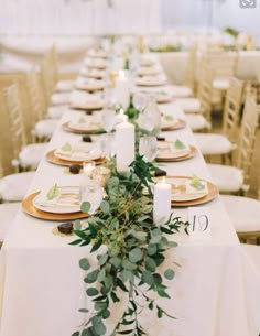 a long table with white linens and greenery is set for an elegant dinner