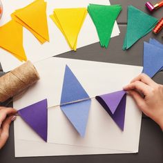 someone is making paper triangles out of construction paper and twine on the table next to them