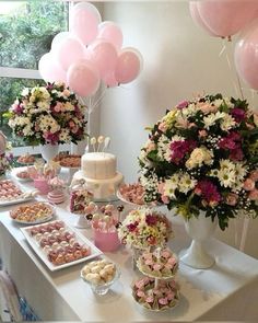 a table topped with lots of pink and white desserts next to tall vases filled with flowers