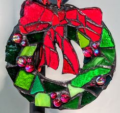 a stained glass christmas ornament hanging from a hook on a white wall with red and green decorations