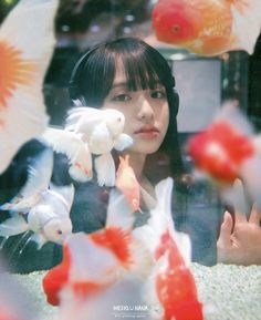 a woman with headphones on looking at goldfish in an aquarium, surrounded by other fish