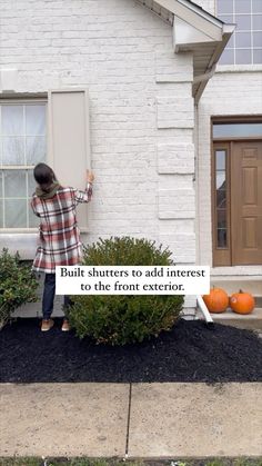 a woman standing in front of a white brick house