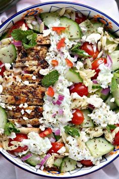 a salad with chicken, cucumber and tomatoes in a blue and white bowl