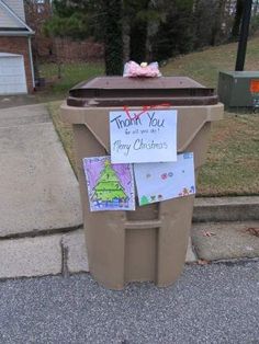 a trash can with a note attached to it on the side of the road next to a mailbox