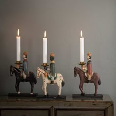 three small figurines are sitting on top of a table with candles in front of them