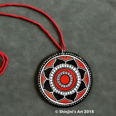 a red and black necklace with a circular design on the front hanging from a red string