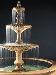 a three tiered fountain with water cascading on the top and bottom, in front of a black background