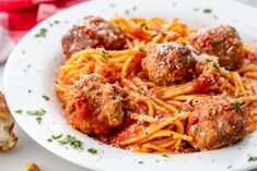 spaghetti and meatballs with tomato sauce on a white plate next to a piece of bread