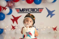 a baby wearing a pilot's hat is sitting in front of a cake