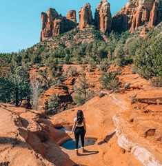 a woman standing on top of a red rock cliff next to a small pool of water