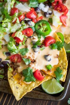 a tray filled with nachos topped with lettuce, tomatoes and black beans