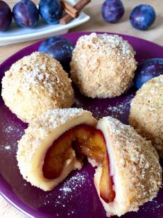 plums and blueberries are cut in half on a purple plate with powdered sugar