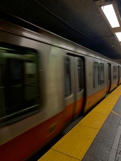 a subway train speeding past a platform with people waiting on the platform to get on