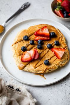 pancakes topped with fruit and syrup on a white plate next to a bowl of strawberries