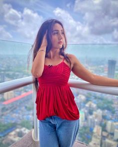 a woman standing on top of a tall building holding her hand to her ear and looking at the camera