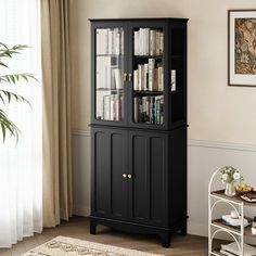 a tall black bookcase with glass doors in a living room next to a window