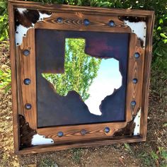 a mirror that is sitting on the ground in front of some grass and bushes with a cowhide pattern around it