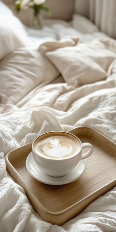 a cup of cappuccino sits on a tray in the middle of a bed