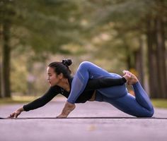 a woman is doing yoga in the middle of an empty road with trees behind her