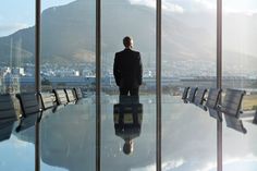 a man standing in front of a conference room table with chairs and mountains in the background